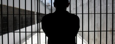 Guarda em pé e contra a luz observa o pátio de um presídio