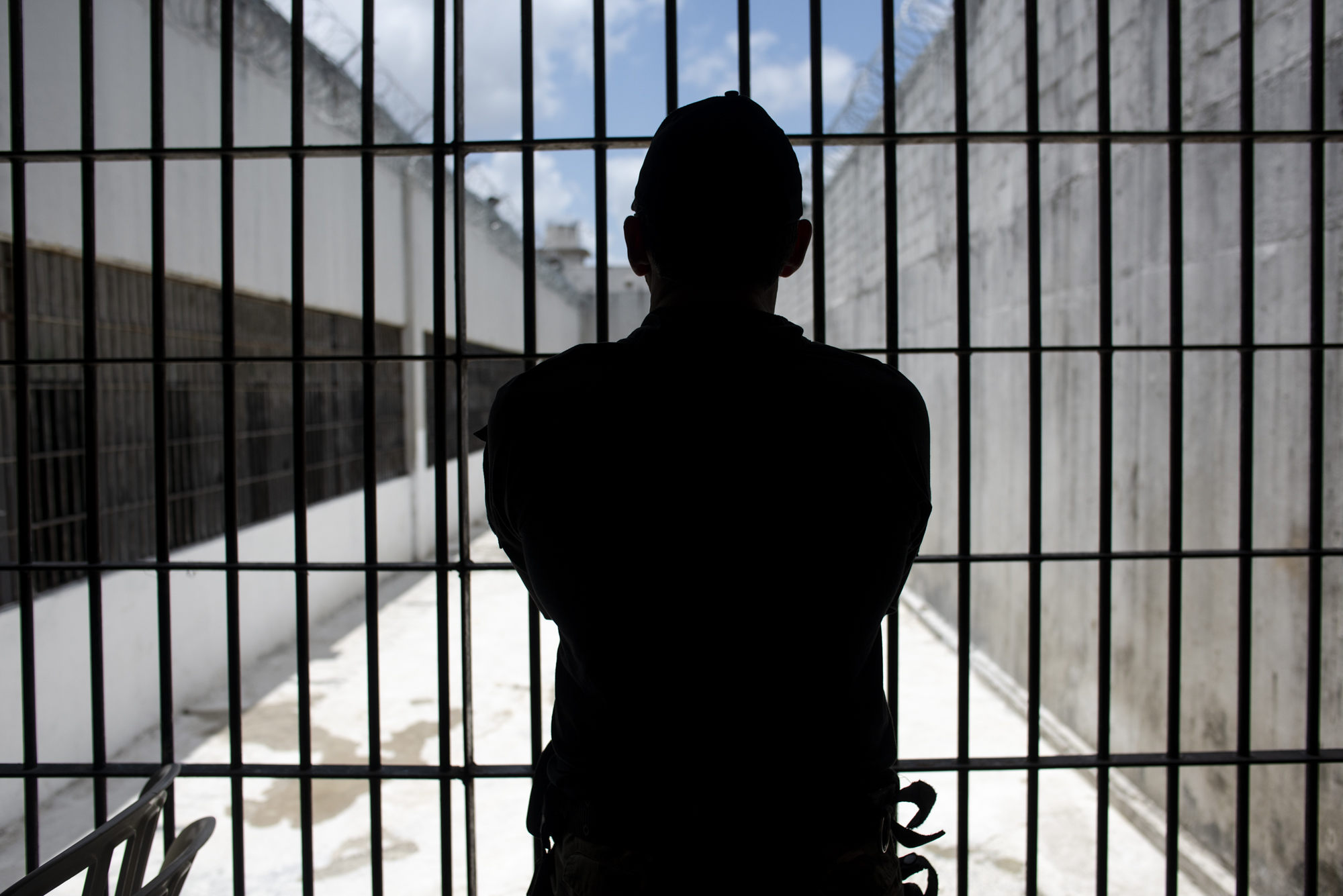 Guarda em pé e contra a luz observa o pátio de um presídio