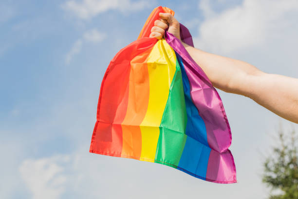 Mão segurando uma bandeira com as cores do arco íris simbolizando a comunidade LGBTQIA+