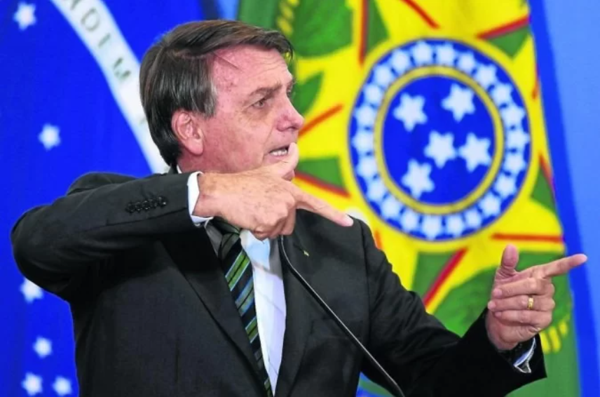 Bolsonaro fazendo arminha com bandeira da República ao fundo