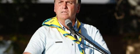 Jair Bolsonaro em ambiente externo com uma bandeira do brasil amarrada no ombro