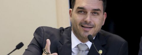 Flávio Bolsonaro com caneta na mão e falando no microfone
