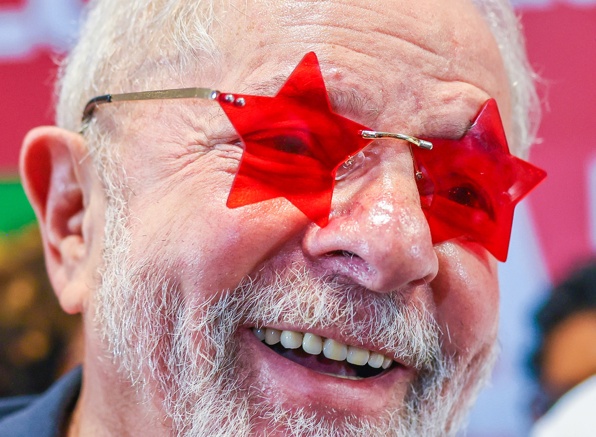 O político Lula sorri e usa um óculos vermelho com as lentes em formato de estrela