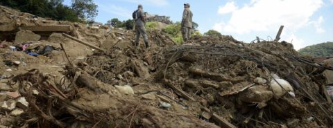 Bombeiros em pé em cima dos escombros avaliam destruição das chuvas