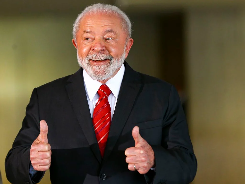 O presidente Lula sorri e faz um sinal de "positivo" com as mãos.