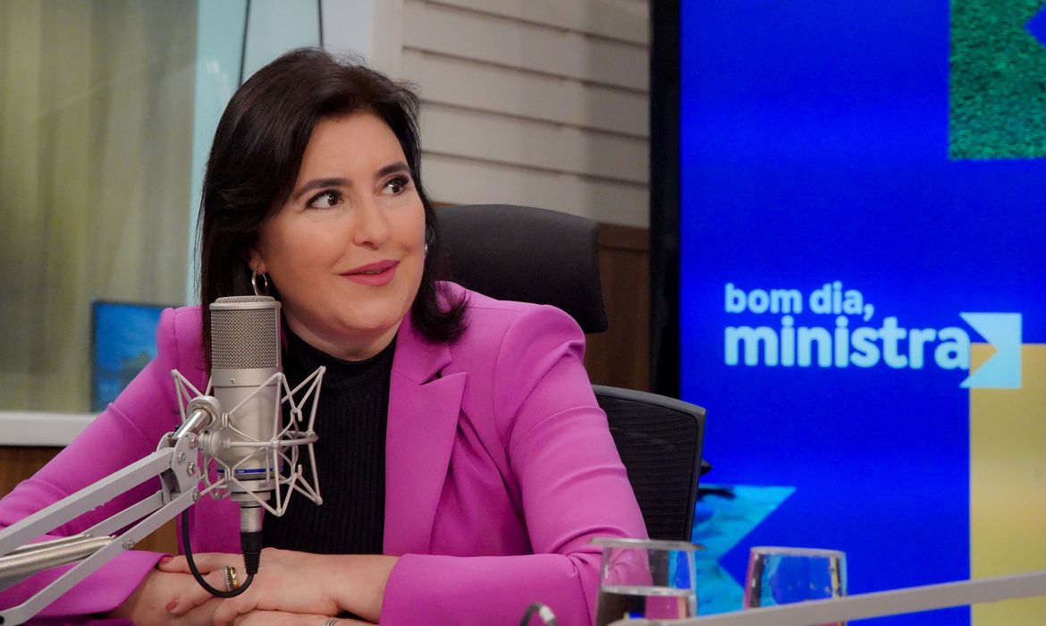 Ministra Simone Tebet durante entrevista ao programa de rádio, diante de um microfone.