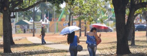 Duas mulheres caminhando pela calçada embaixo do guarda-sol