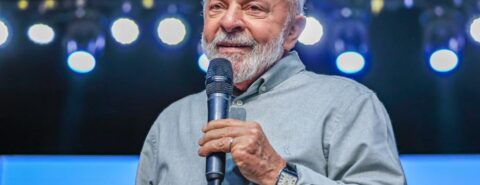 Presidente Lula, vestindo uma camisa cinza, fala ao microfone.