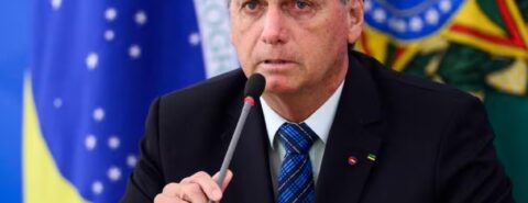 Jair Bolsonaro de terno e bandeira do Brasil ao fundo