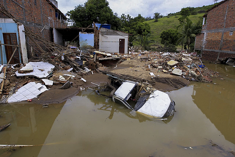 Handout picture released by the Bahia State Government showing a semi submerged car and debris next to a house destroyed during a flood caused by heavy rains in the region, in Ubaira, south of Bahia State, Brazil, on December 30, 2021. - The death toll from heavy rains and floods that plagued the northeastern Brazilian state of Bahia since November rose to 24 on December 29, amid incessant torrents that have displaced almost 90,000 people and left a trail of destruction in several municipalities, authorities said. (Photo by Fernando VIVAS / Bahia State Government / AFP) / RESTRICTED TO EDITORIAL USE - MANDATORY CREDIT "AFP PHOTO / BAHIA STATE GOVERNMENT / FERNANDO VIVAS" - NO MARKETING - NO ADVERTISING CAMPAIGNS - DISTRIBUTED AS A SERVICE TO CLIENTS