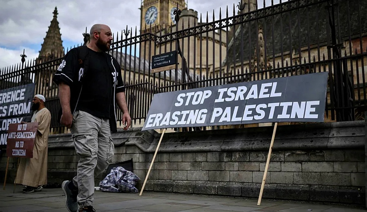 Homem passa por um cartaz de protesto contra Israel, próximo ao Parlamento Britânico, em Londres, 9 set. 2026 \ Créditos: AFP/HENRY NICHOLLS