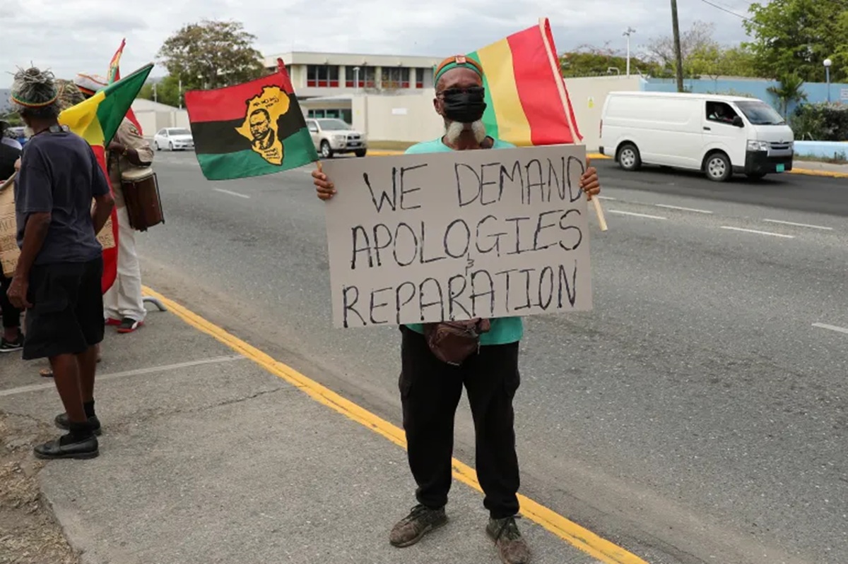 Um manifestante segura um cartaz durante um protesto exigindo que o Reino Unido pague reparações pela escravidão, antes da visita do Duque e da Duquesa de Cambridge à Jamaica, em Kingston, Jamaica [Arquivo: Gilbert Bellamy/Reuters] - 
Reprodução